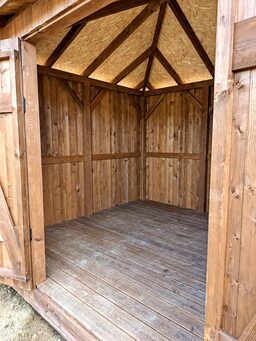 An empty wooden shed with open doors and a wooden floor.