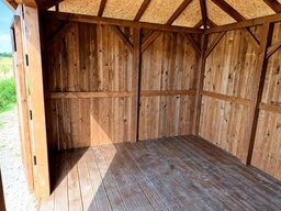 An empty wooden shed with walls and a wooden floor, illuminated by sunlight.
